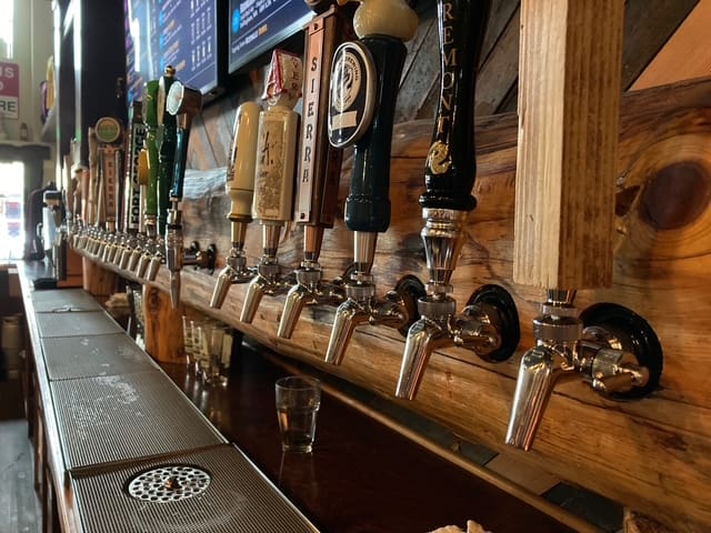 A row of beer tap handles mounted on a wooden board above a bar counter.